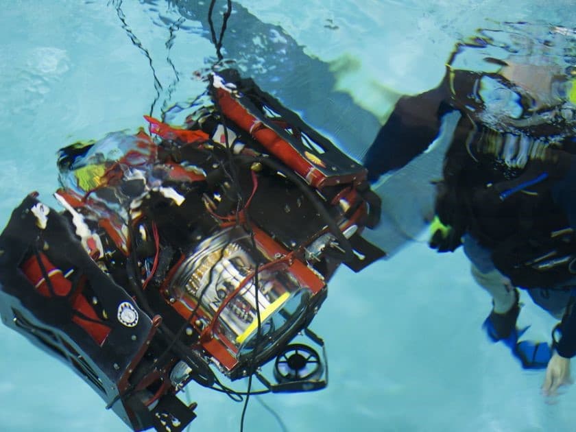 Two people in a pool with a robot in the water.