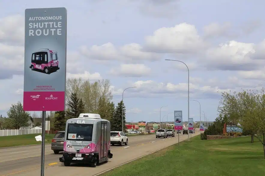 A pink car driving down a road with a sign on it.