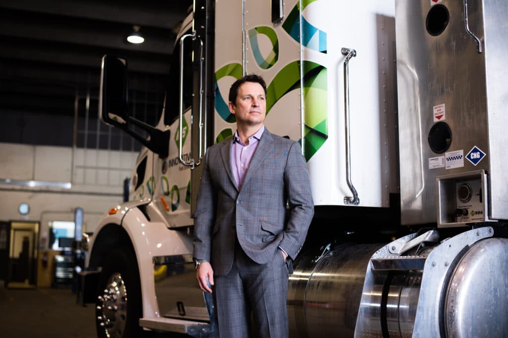 A man in a suit standing in front of a semi truck.