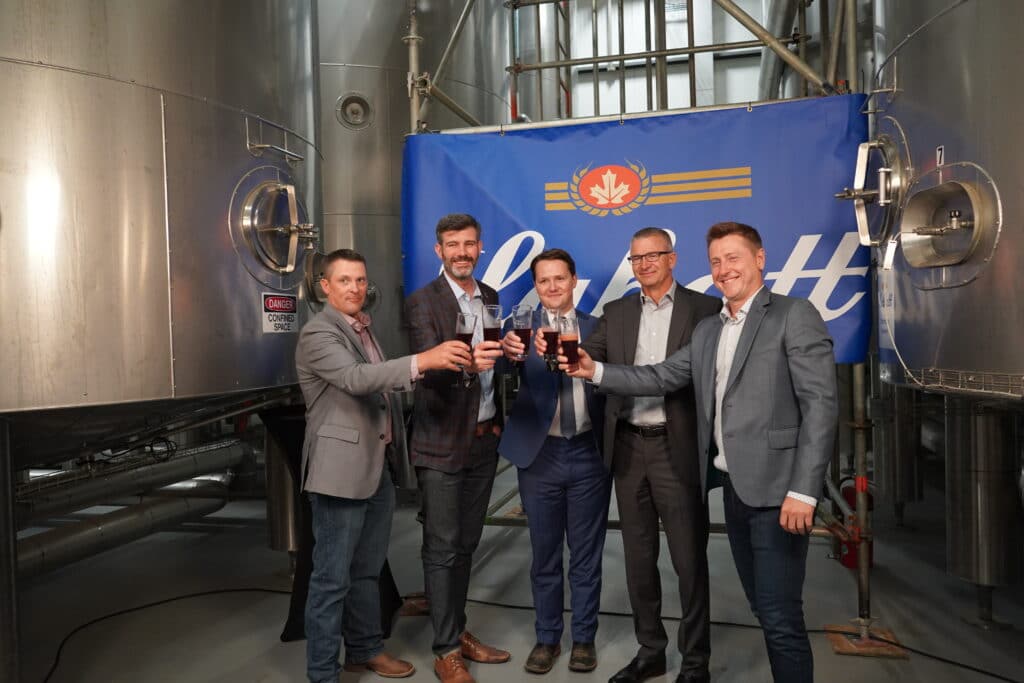Four men in suits standing in front of a brewery.