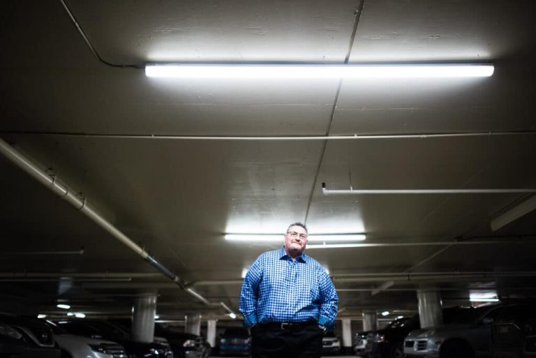 A man standing under a light in a parking garage.