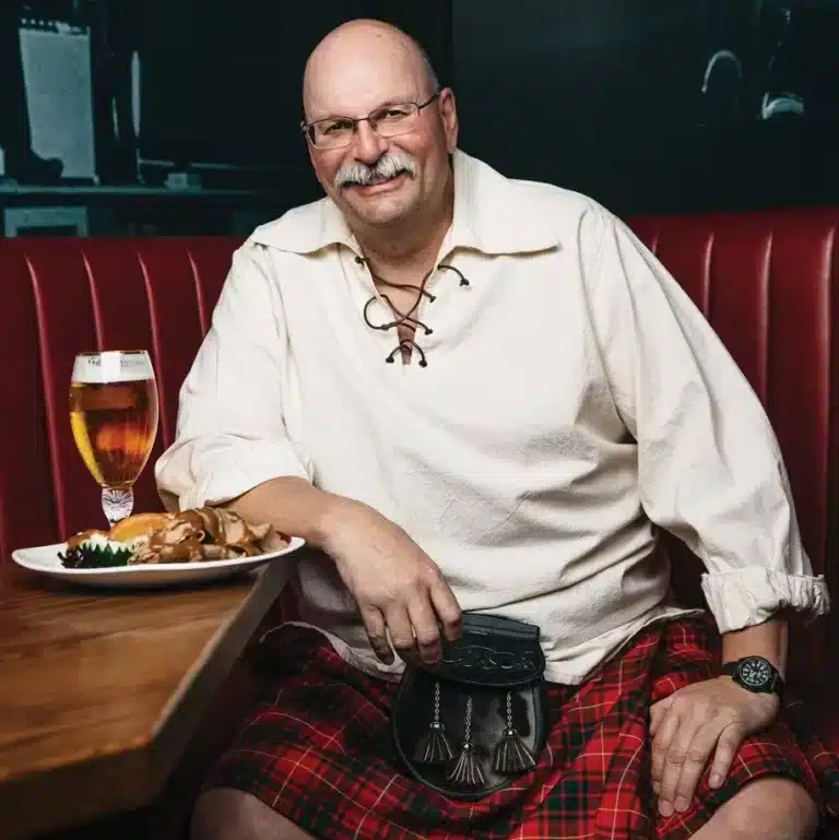 Malcolm Bruce in a kilt sitting at a table with food.