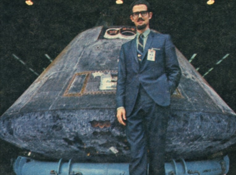 A man in a suit standing next to a space shuttle.