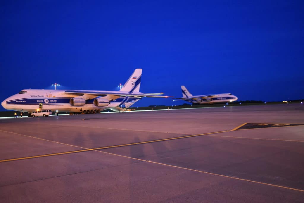 Two large airplanes parked on the tarmac at night.