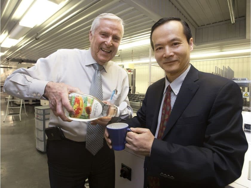 Two men in suits standing next to a plate of food.