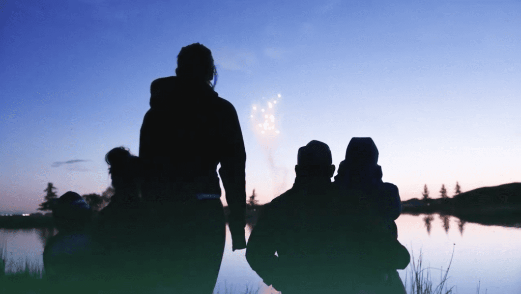 Silhouettes of a family watching fireworks at dusk.