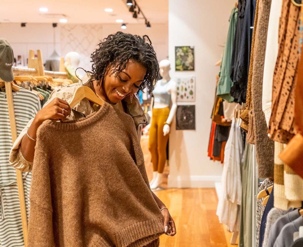 A woman looking at a sweater in a clothing store.