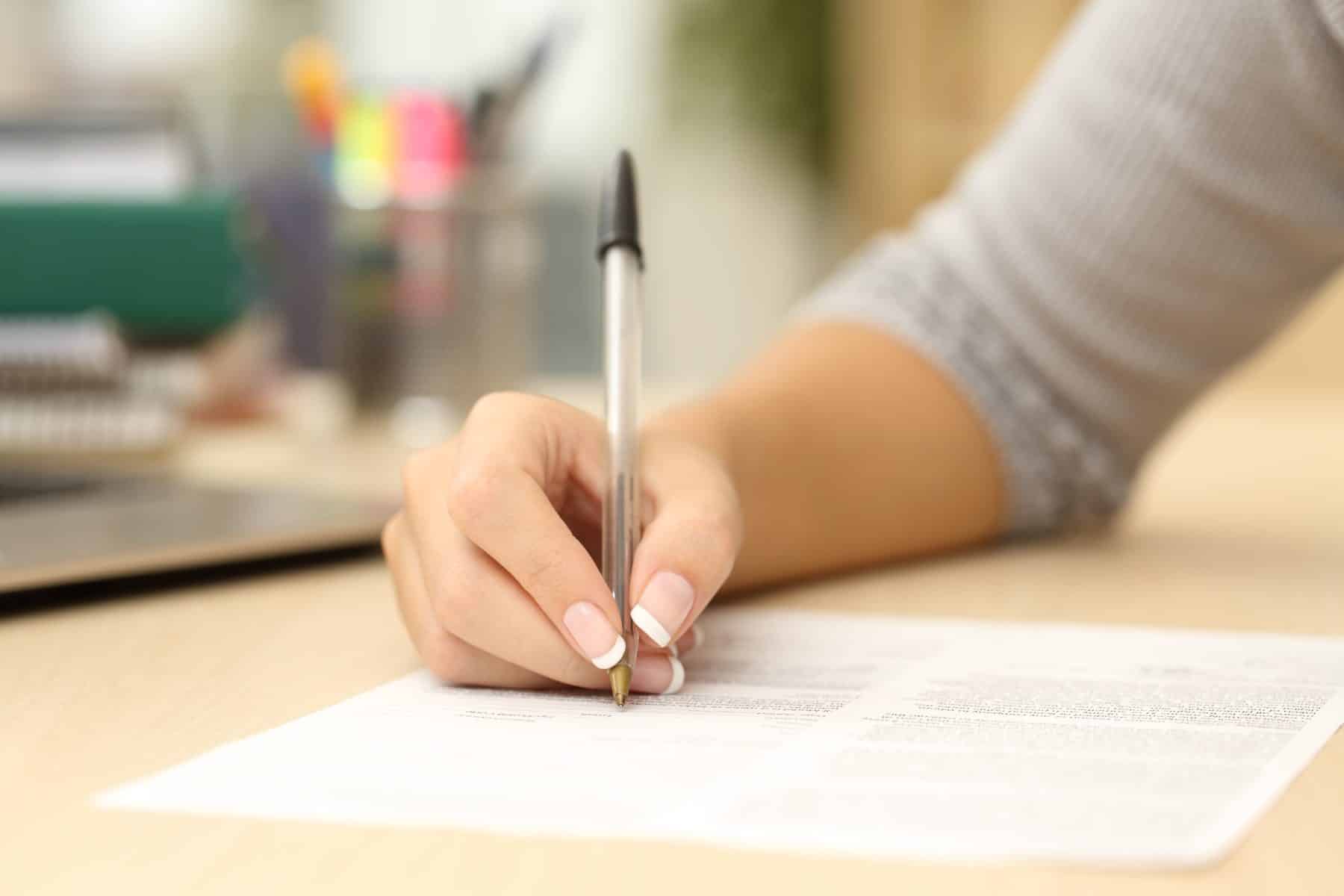 A woman writing on a piece of paper with a pen.