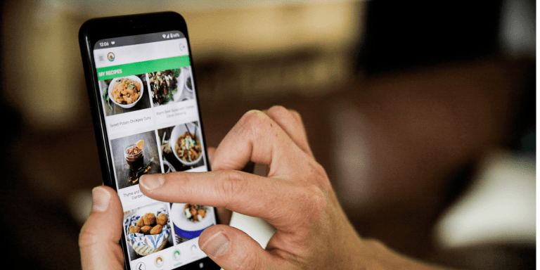 A person holding up a smartphone with pictures of food on it.